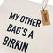Beige tote bag with black text 'My other bag's a Birkin' and a visible brand tag.