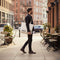 Man walking on a city street with a tote bag labeled 'S.B.C.'