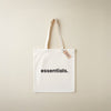 White tote bag with 'essentials.' text and a tag on a beige background