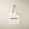 White tote bag with 'essentials.' text and a tag on a beige background