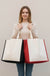 Four colorful tote bags (yellow, red, blue, orange) hanging on a rack against a white wall.